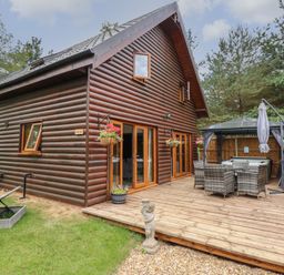 Exterior view of a wooden lodge with a deck patio table chairs gazebo and hanging flower baskets at Little Lodge in Pentney near King's Lynn