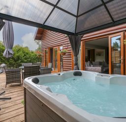 An outdoor deck with a hot tub under a gazebo and a dining table with wicker chairs at Little Lodge in Pentney near Kings Lynn