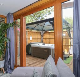A room with a potted plant and grey curtains looking out through glass doors to a wooden deck with a covered hot tub at Little Lodge in Pentney near King's Lynn