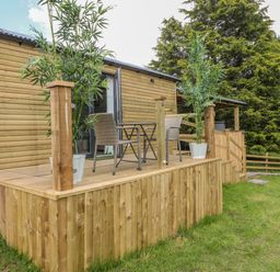 An outdoor wooden deck with two wicker chairs and a table in front of a wooden cabin at High Rigg Shepherd's Sunrise in Brampton Cumbria