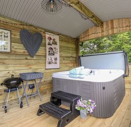 A covered wooden patio with a hot tub steps and a small grill at High Rigg Shepherd's Sunrise in Brampton Cumbria