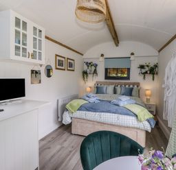 A bedroom with a bed towels and pillows a television on a cabinet and chairs with flowers at High Rigg Shepherd's Sunrise in Brampton Cumbria