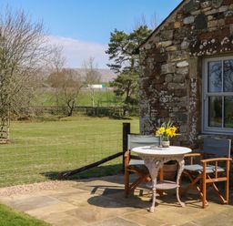 An outdoor stone patio with a small round table and two chairs next to a stone building at Herdie Hideaway in Appleby-In-Westmorland