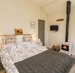 A bedroom with a bed a wood stove a mounted television and a side table at Herdie Hideaway in Appleby-In-Westmorland