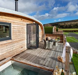 An outdoor wooden deck with a table and two chairs and a hot tub adjacent to a wooden cabin at Middle Longlands in Cartmel