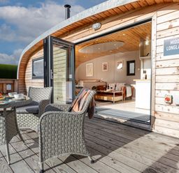 An outdoor seating area with a table and chairs on a wooden deck opening into an indoor living space at Middle Longlands in Cartmel