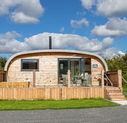 A curved wooden cabin with a front porch, chairs and table outside at High Longlands in Cartmel