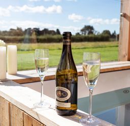 A bottle of prosecco with two glasses of water on the edge of a wooden hot tub at High Longlands in Cartmel