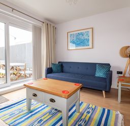A living room with a blue sofa two cushions a wooden coffee table a side table with a lamp and striped rug at 6 Ocean Heights in Newquay