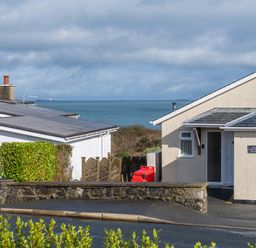 A view of houses with a stone wall and ocean in the background at Cartref in Benllech