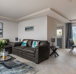 A living room with two sofas a coffee table with flowers and champagne glasses and a dining area with chairs and a table at Cartref in Benllech