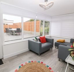 A sunroom with gray armchairs and a sofa with red and patterned cushions a round jute rug and a white side table with a potted plant at Daresfield in Cemaes Bay