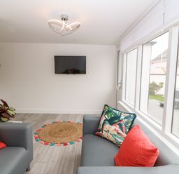 A sitting room with two grey sofas with red and patterned cushions a round woven rug mounted television and large windows at Daresfield in Cemaes Bay
