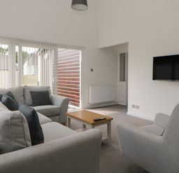A living room with a grey sofa set a wooden coffee table and a wall-mounted television at Harcombe House Bungalow 11 in Chudleigh