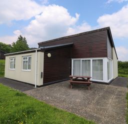 A bungalow with a patio and picnic table on a grassy lawn at Harcombe House Bungalow 11 in Chudleigh