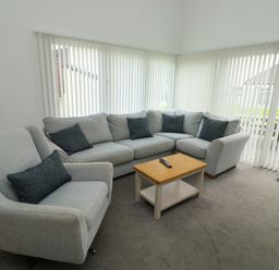 A living room with a grey armchair and an L shaped sofa with dark cushions and a wooden coffee table with a remote at Harcombe House Bungalow 11 in Chudleigh