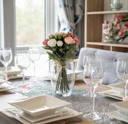 A dining table set with white square plates and wine glasses with a flower centerpiece at Loluke Lodge on The Lake 5 Coniston Drive Borwick near Carnforth