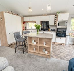 A kitchen with an island and two stools next to a window at Loluke Lodge on The Lake 5 Coniston Drive Borwick near Carnforth