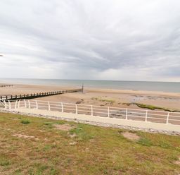 A sandy beach with sea defenses and a walkway with railings at Ty Uchaf in Rhyl
