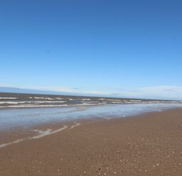 A sandy beach with waves and a clear blue sky at Ty Uchaf in Rhyl