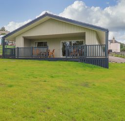 A house with a porch and wooden furniture overlooking a grassy lawn at The Lodge in Blairgowrie