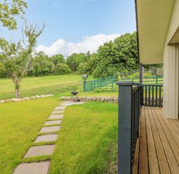 A backyard with a wooden deck a pathway leading to a barbecue grill and trees at The Lodge in Blairgowrie