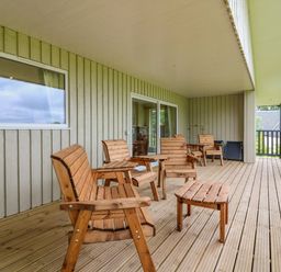 A covered wooden deck with wooden chairs and tables outside a house at The Lodge in Blairgowrie