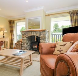 A living room with leather armchairs a wooden coffee table a stone fireplace and two windows at The Lodge in Blairgowrie