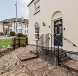 The entrance of a building with stone steps and a black door next to a window and a grassy area at 2 Old Talbot Cottages in Lostwithiel