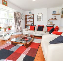 A living room with white sofas red and black cushions a patterned rug glass coffee tables a bookshelf and large windows at 2 Old Talbot Cottages Lostwithiel