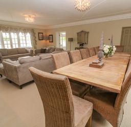 A dining area with a wooden table and upholstered chairs next to a seating area with sofas and armchairs in a large room at Bodmin Country House in Lanivet