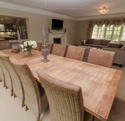 A dining room with a long wooden table and chairs next to a living area with sofas and a fireplace at Bodmin Country House in Lanivet