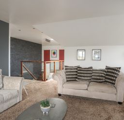 A living room with two sofas and a coffee table near a staircase with a glass railing at The Old Coal Yard in Cemaes Bay