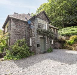 A stone house with gravel driveway surrounded by plants and trees at Huntingstile Lodge in Grasmere