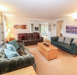 A living room with three sofas a wooden coffee table and landscape paintings at Huntingstile Lodge in Grasmere