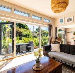 A living room with a sofa table and large windows looking out to a garden at Chi Lowarth in Porthleven