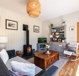 A living room with a sofa a rocking chair a wood stove a wooden coffee table and a grey cabinet at Chi Lowarth in Porthleven