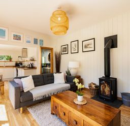 A living room with a gray sofa and wood stove next to a wooden coffee table at Chi Lowarth in Porthleven