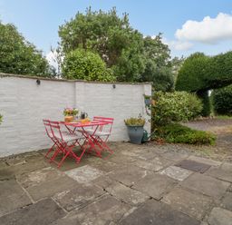 An outdoor patio area with a red table and four chairs a white wall and green plants at Pentre Court Cottage in Abergavenny