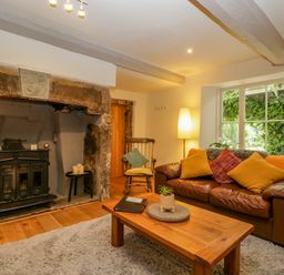 A living room with a leather sofa cushions a wooden coffee table and a fireplace at Pentre Court Cottage in Abergavenny