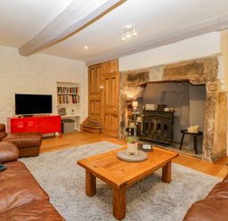 A sitting room with leather sofas a wooden coffee table a tv on a red cabinet and a fireplace at Pentre Court Cottage in Abergavenny