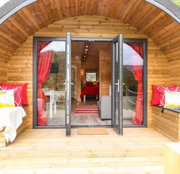 A wooden pod with open glass doors showing a bed and seating area inside at Hartsop Magic - Crossgate Luxury Glamping in Hartsop near Glenridding