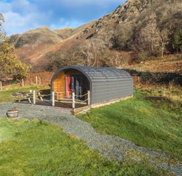 A small cabin with a curved roof next to a picnic table on grass with hills and trees in the background at Hartsop Magic - Crossgate Luxury Glamping in Hartsop near Glenridding