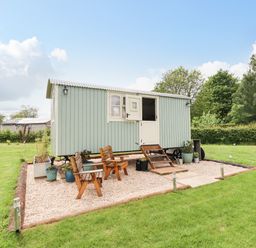 A small light blue wooden cabin with a split door on a gravel patio with wooden chairs and potted plants at Honeybee Lodge in Stixwould near Woodhall Spa