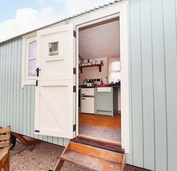 A wooden exterior door open to show a small kitchen with a fridge kettle and sink at Honeybee Lodge in Stixwould near Woodhall Spa