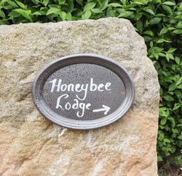 A black oval sign with Honeybee Lodge written on it attached to a large stone with green bushes behind at Honeybee Lodge in Stixwould near Woodhall Spa