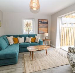 A living room with teal sectional sofa and patterned armchair near a wooden coffee table and sliding glass door at 1 Crud Y Mor in Barmouth