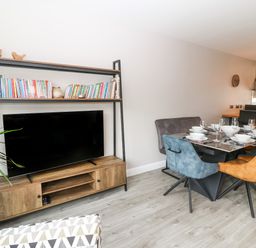 A living room with a television on a wooden stand and a dining table with chairs set with dishes at 1 Crud Y Mor in Barmouth