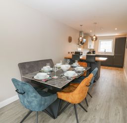 A dining table set with plates and glasses next to a kitchen with pendant lights and seating at 1 Crud Y Mor in Barmouth