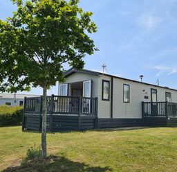 A mobile home with a wooden deck and a tree in the yard at Vendee Lodge Thorness Bay Holiday Park near Cowes